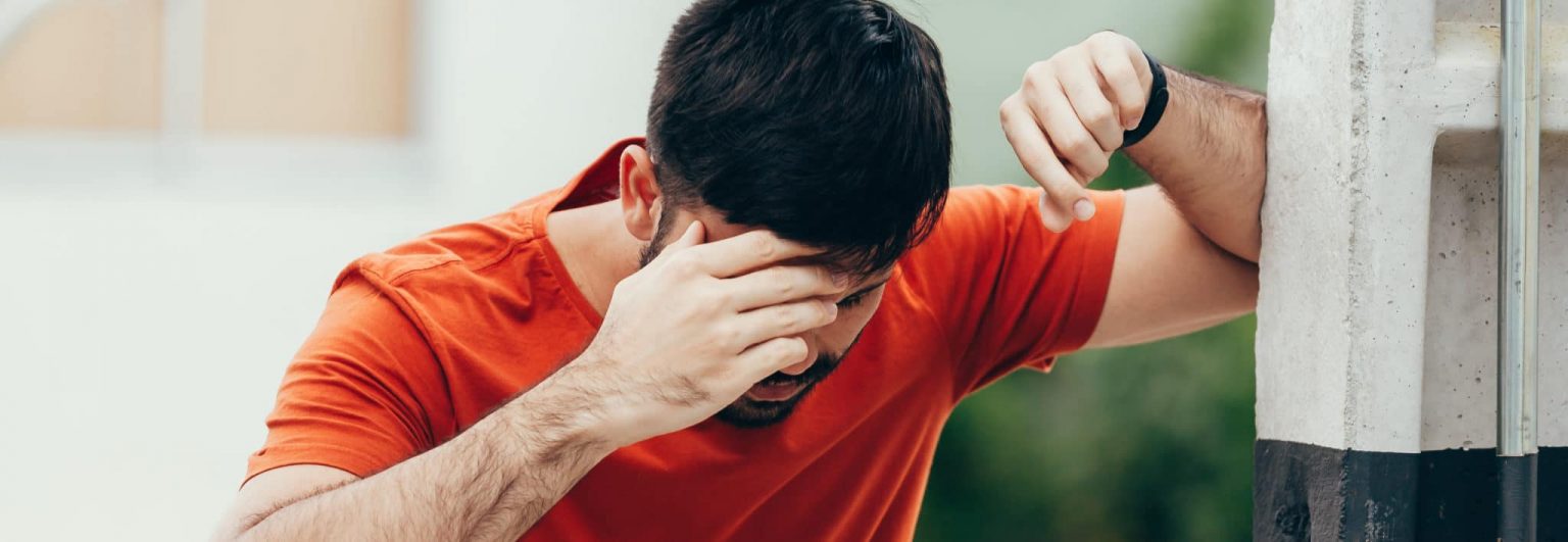 man resting elbow against wall and holding head to stop dizziness