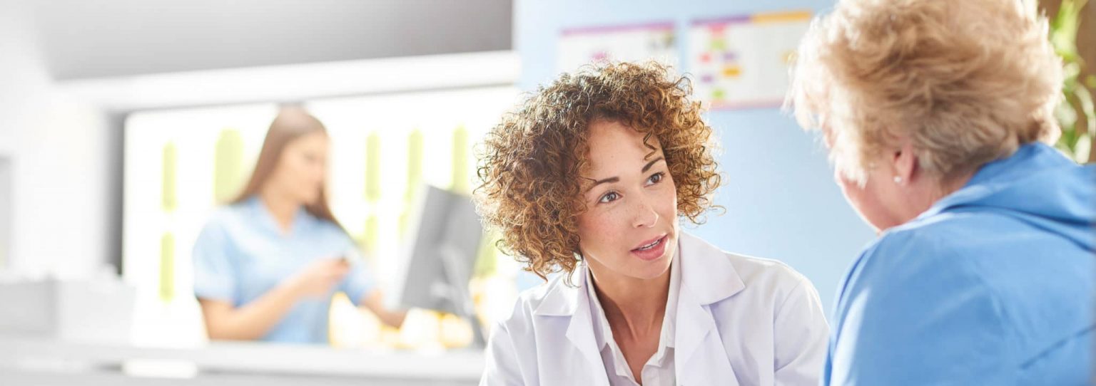 Doctor discussing voice disorders with patient with a nurse in the background entering patient information.