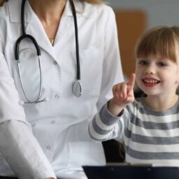 Close-up of smiling child pointing finger and holding paper folder. Happy kid looking at camera with gladness and smiling. Healthcare and prevention concept