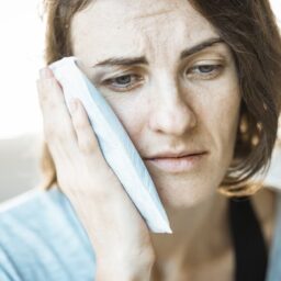 A woman holding an ice pack to her face to relieve TMJ pain.