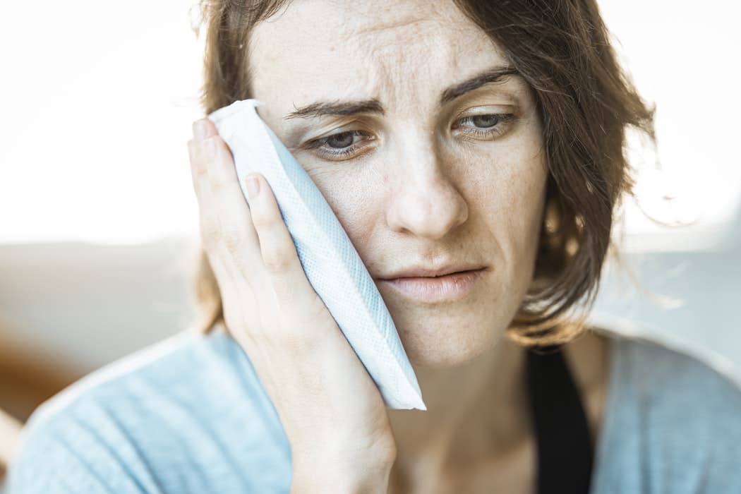 A woman holding an ice pack to her face to relieve TMJ pain.