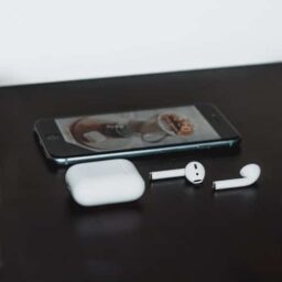A smartphone next to a pair of wireless earbuds.