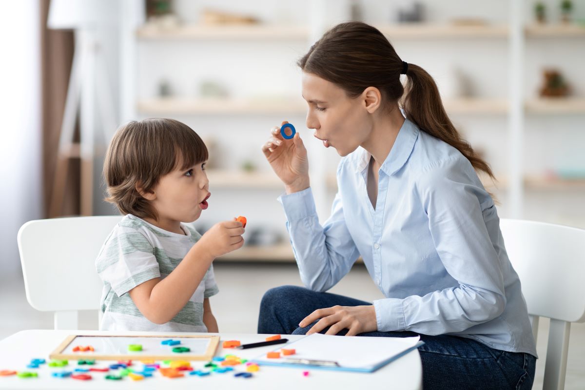 woman providing verbal therapy to a child - woman is holding up the letter o and the child is is mimicking the woman as they both practice the sound