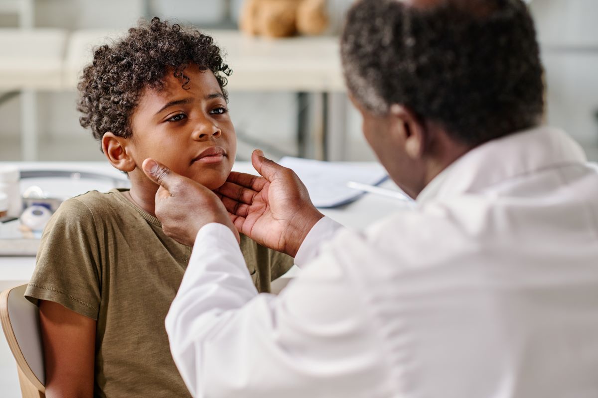 Doctor in clinical setting feeling a child's throat area as part of a diagnosis