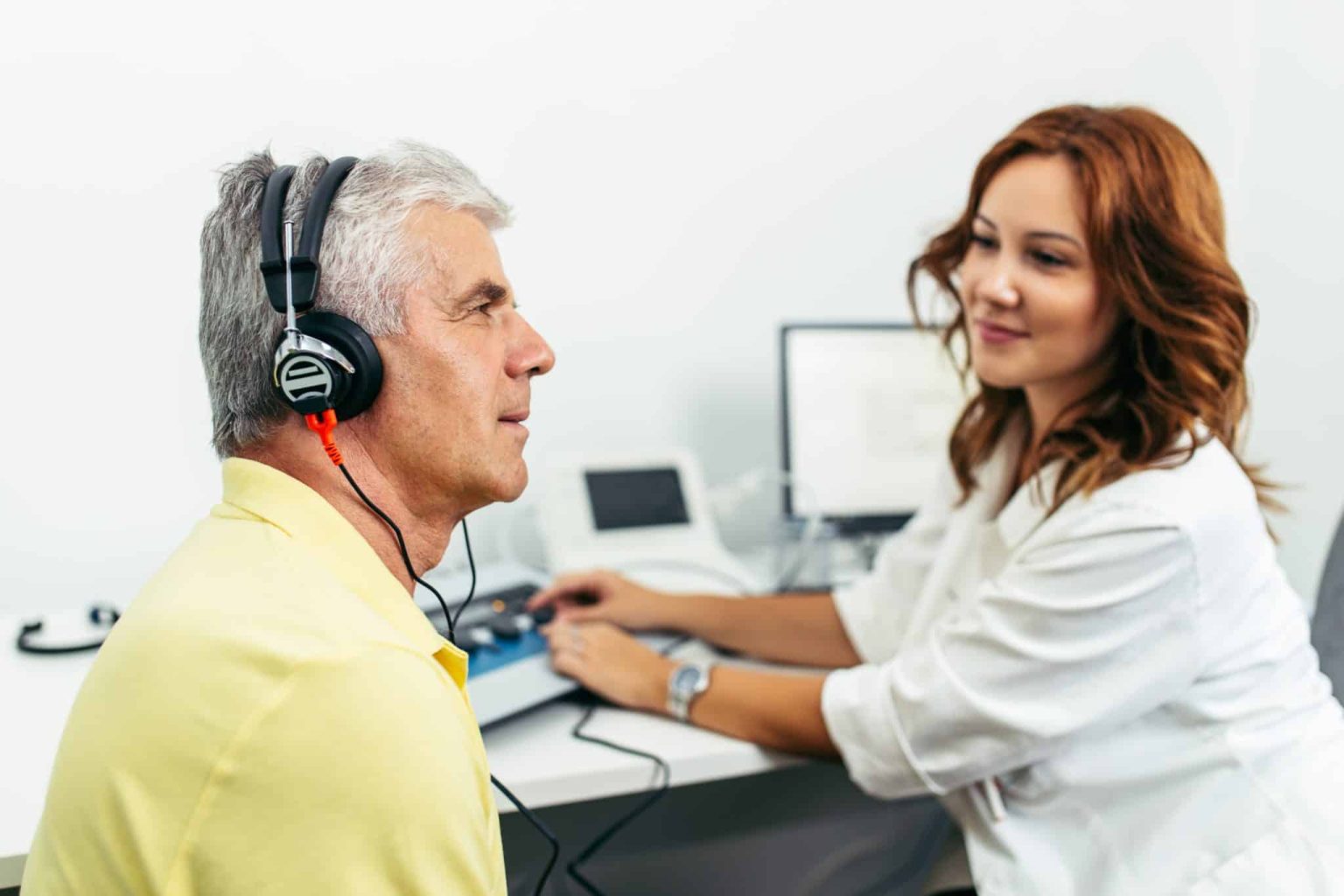 Man in an audiologists office with headphones on listening intently during a hearing test