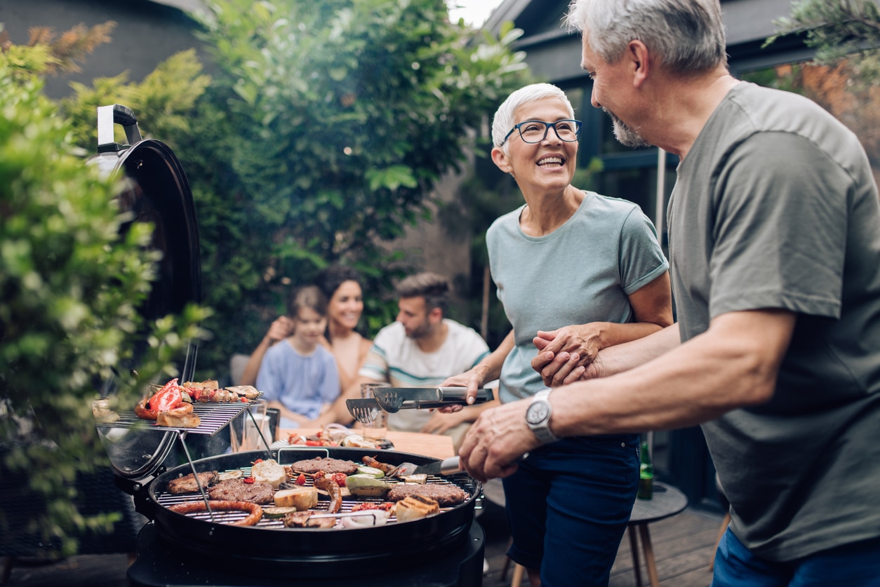 Man and woman standing at a grill at a small barbecue.