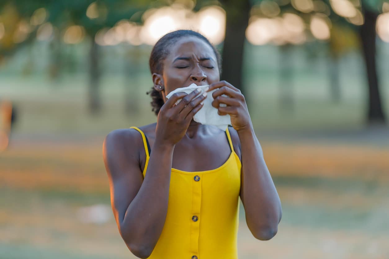 Woman sneezing into a tissue at the park