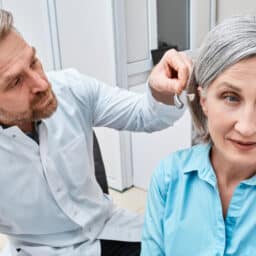 Audiologist fitting a woman with a new hearing aid