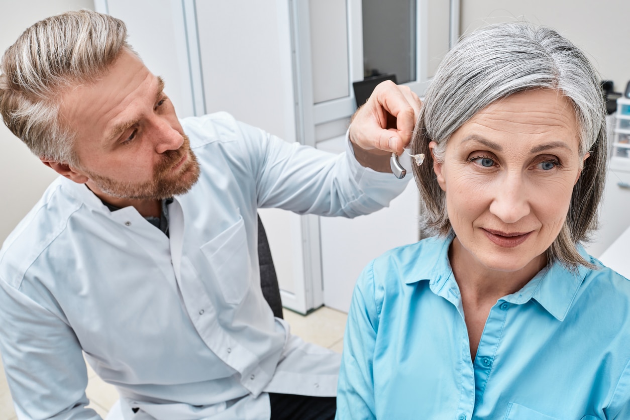 Audiologist fitting a woman with a new hearing aid.