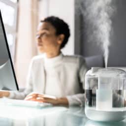 Woman working at her desk, running a humidifier next to her.