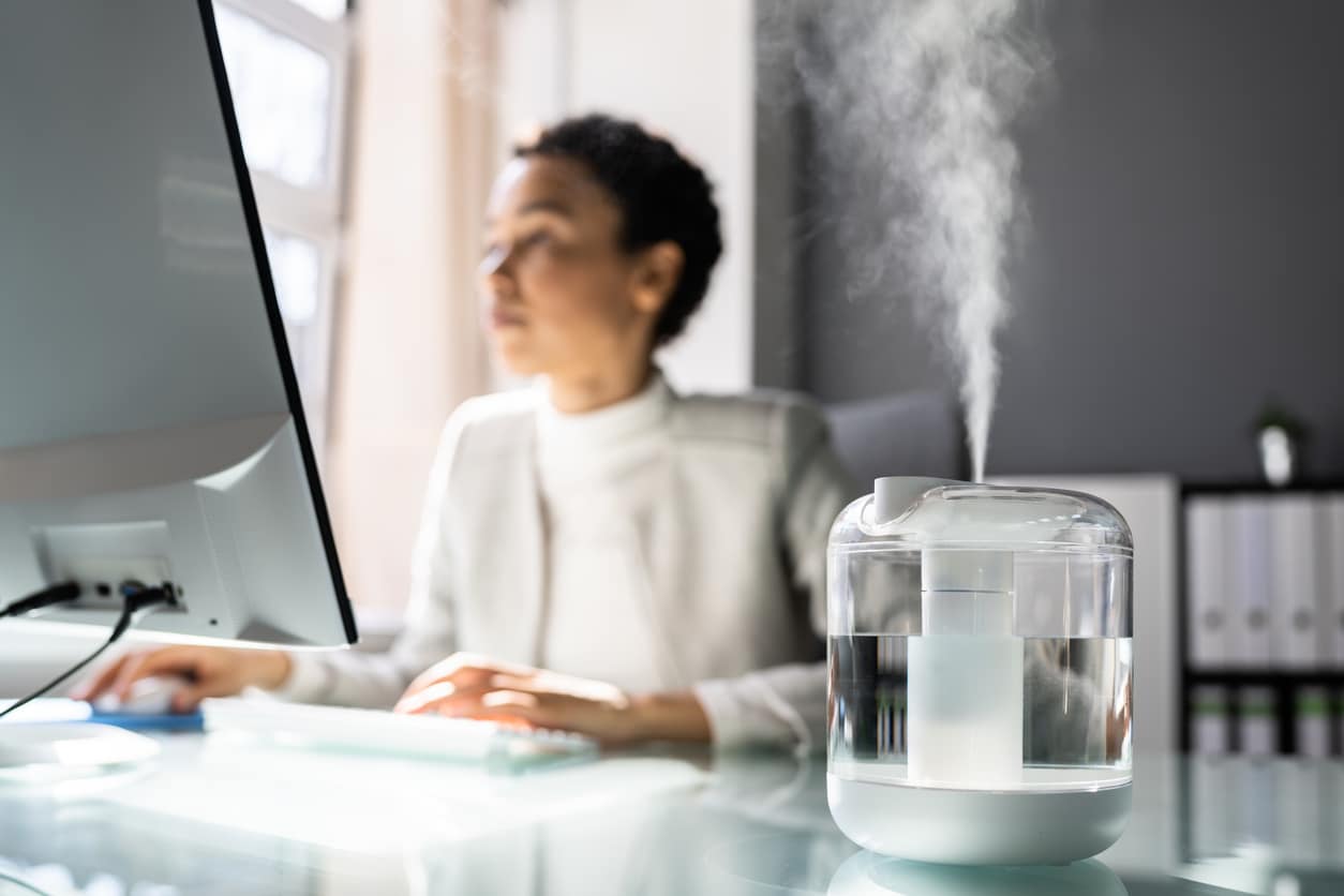 Woman working at her desk, running a humidifier next to her.