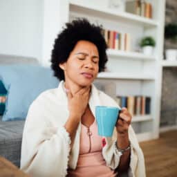 Woman drinking tea holding her sore throat