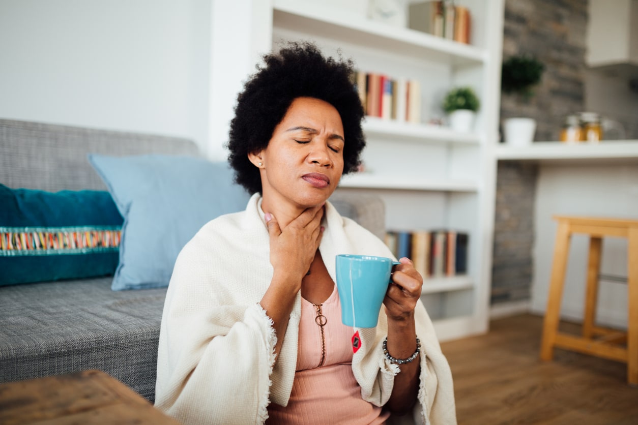 Woman drinking tea holding her sore throat.