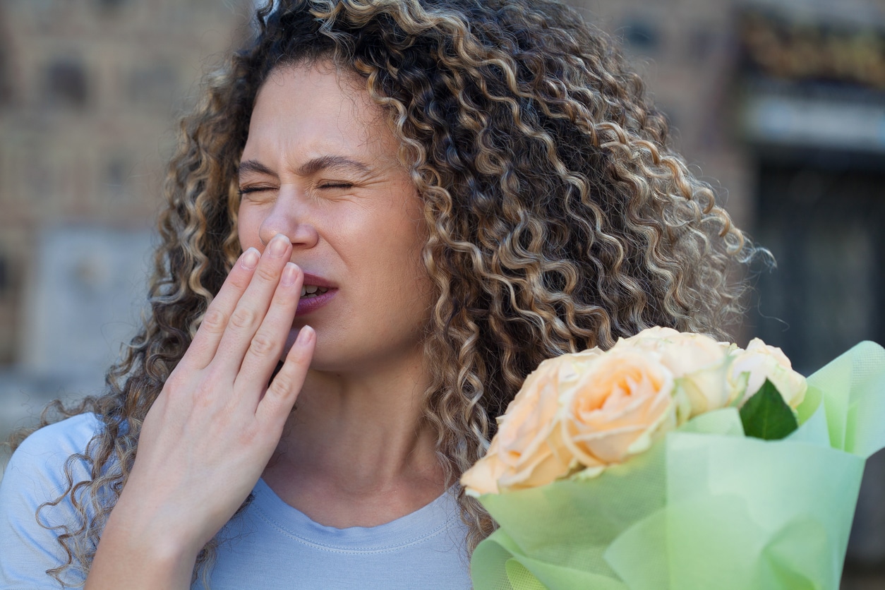 Woman holding flowers trying not to sneeze.