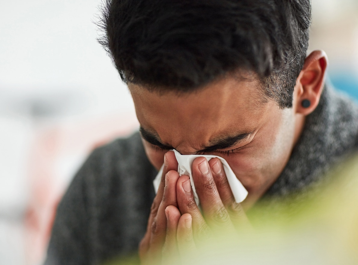 Man holding tissue to nose sneezing