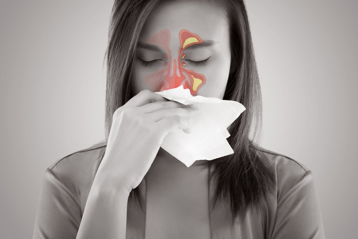 Woman with a sinus infection blows her nose; an illustration of the infected sinus cavities is superimposed over her face.